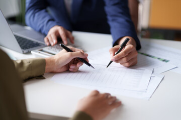close-up of two individuals discussing and pointing at a document on a desk. the hands are holding p