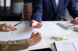 © STBSTD - Two individuals engaged in a discussion at a desk, with a focus on their hands and a document. A laptop displaying charts and graphs is visible in the background.