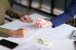 © STBSTD - Two individuals engaged in a discussion at a desk, with a focus on their hands and a document. A laptop displaying charts and graphs is visible in the background.