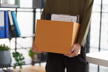 A person carrying a box filled with office supplies, including a clipboard and folders. The scene suggests a move or transition, possibly related to a job change.