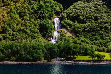 Sticker - Scenic view of Odnesfossen waterfall cascading down a lush green mountainside in Styvi, Norway