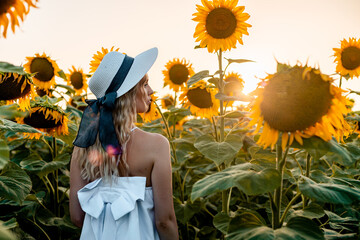 Woman In White Dress Stands In Field Of Sunflowers At Sunset