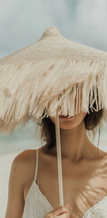 Wall Mural - A woman partially hidden by a straw umbrella at the beach. Minimal summer fashion concept.