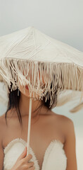 Wall Mural - A woman partially hidden by a straw umbrella at the beach. Minimal summer fashion concept