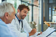 © SensSai/peopleimages.com - Hospital, doctor and people with clipboard in discussion for health insurance, planning and info. Men, patient and consultation with checklist at desk for premium option, coverage or medical benefits