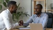 © Creations Photo  - Two diverse businessmen at office meeting shake hands after successful business contract agreement. African businessman signing paper document offer Caucasian man salesman handshake client customer.
