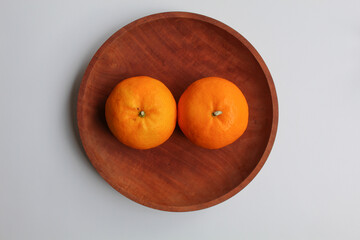 Two orange fruits, served on wooden plate, isolated on white background, flat lay or top view