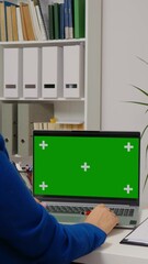Vertical Screen: Woman sitting working on laptop with mock up green screen chroma key display. Freelancer using isolated laptop browsing on internet for social media advertising.