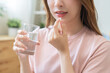 © KMPZZZ - Dietary supplement, healthy diet positive asian young woman hand holding pill capsule, take vitamin in mouth for beauty skin hair, taking medicine with glass of water at home, pharmacy and health care