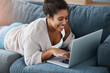 © Sanc/peopleimages.com - Woman, typing and laptop on sofa in house, smile and communication on dating site or virtual contact. Connection, social media and online shopping or customer browsing, internet and streaming video
