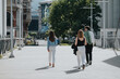 © qunica.com - Three individuals walking on a city street bathed in daylight, showcasing a modern urban environment with buildings and greenery.