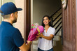 © AntonioDiaz - Young delivery man presenting a bouquet of flowers to a young woman at her doorstep