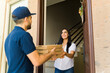 © AntonioDiaz - Smiling delivery man carrying a pizza order in cardboard boxes to woman at front door