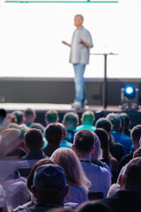 Wall Mural - Focused audience attentively listening to a speaker delivering a presentation at a business conference or seminar. Ideal for concepts such as learning, professional development, and networking.