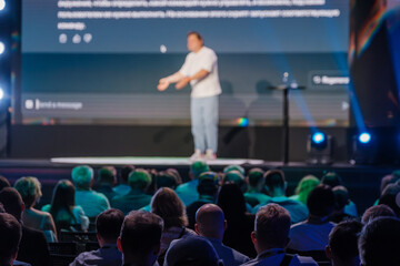 Wall Mural - Speaker giving an engaging presentation to a seated audience at a conference. The audience is attentively listening and the atmosphere is professional.