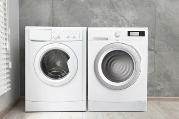 Two washing machines near tiled wall in laundry room