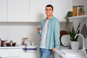 Wall Mural - Handsome young man with cup of coffee in kitchen at home