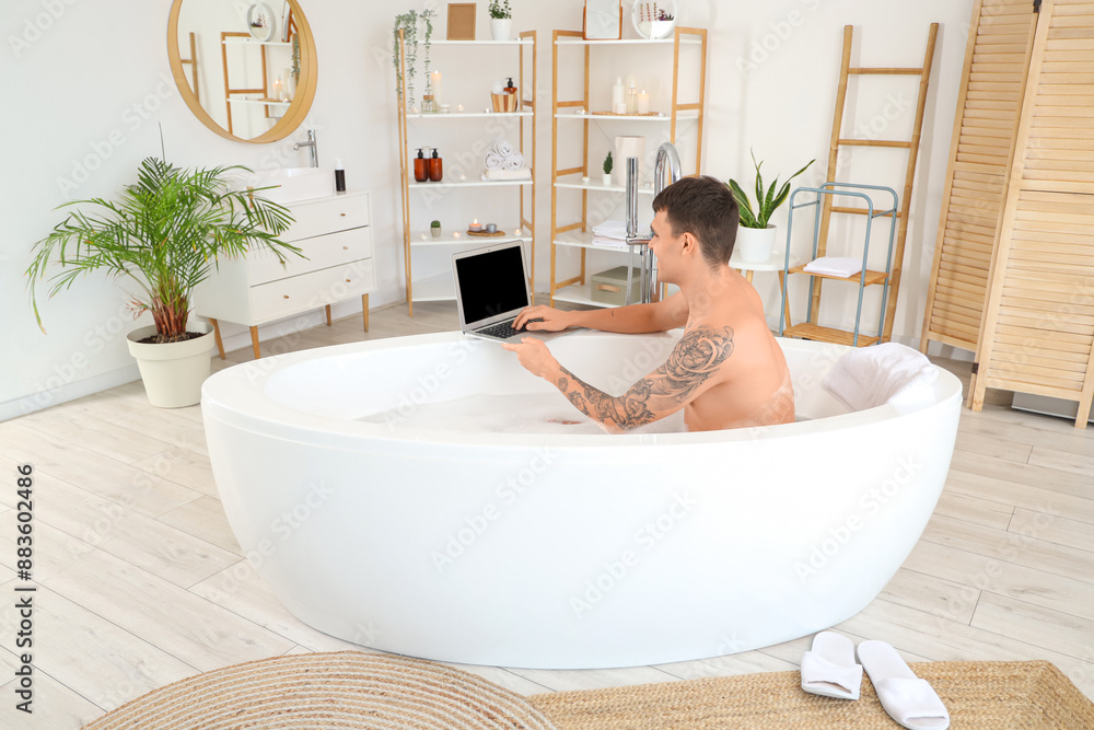 Young man with laptop taking bath at home