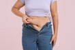 © Pixel-Shot - Overweight woman in tight jeans on pink background. Excess weight concept