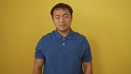 Poster - Young chinese man standing and winking with a happy, cheerful face looking at the camera with a sexy expression, over an isolated yellow background