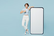 © ViDi Studio - Full body young happy woman wears striped t-shirt casual clothes big huge blank screen mobile cell phone smartphone with mockup area show thumb up isolated on plain blue background. Lifestyle concept.