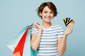 Wall Mural - Young woman wears striped casual clothes hold in hand paper package bags after shopping hold many credit cards isolated on plain light pastel blue color background. Black Friday sale buy day concept.