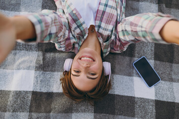 Top view close up young woman wear casual clothes headphones listen music doing selfie shot pov mobile cell phone lay down on plaid rest on sea sand shore in summer day free time. Lifestyle concept.