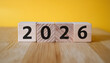 © hardvicore - Wooden cubes with number 2026 on yellow backdrop. New year. Wood blocks. Close-up.
