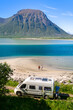 © Fokke Baarssen - A couple walks hand-in-hand on a pristine beach, a campervan parked nearby, with a majestic fjord and mountain backdrop. motorhome at the beach of Lofoten Norway