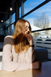 © Anastasiia - The image depicts an individual sitting at a well-lit cafe table. Sunlight streams through large windows, creating a cozy ambiance.