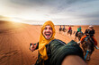 © Davide Angelini - Happy tourist having fun enjoying group camel ride tour in the desert - Travel, life style, vacation activities and adventure concept