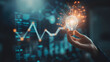 © narumon - Hand holding a glowing light bulb in front of a business graph It is a symbol of innovation and new ideas.