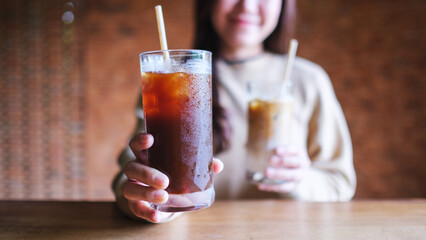 Wall Mural - Closeup image of a young woman holding and serving two glasses of iced coffee