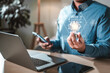 © Day Of Victory Stu. - innovative, drawing, power, lightbulb, creativity, brainstorm, global, imagination, invention, future. A man is holding a cell phone and a laptop, and a light bulb with the word AI above it.