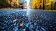 © kaleidoscope - A close-up of freshly laid asphalt on a road, with fall foliage blurred in the background