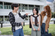 © amnaj - Young man points animatedly while talking to two female students on a bustling university campus, symbolizing modern social interaction in an educational setting