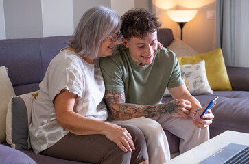 Sticker - Smiling handsome boy and his grandmother sitting together on sofa using telephone smartphone technology for online webcam connection