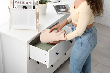 Poster - Beautiful young African-American woman putting clean clothes into commode at home, closeup