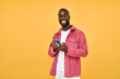 © insta_photos - Young happy smiling African American Black hipster man wearing red shirt with cellphone standing isolated on yellow background holding smartphone using mobile cell phone technology looking at camera.