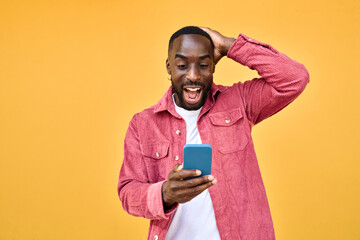 excited black man looking at smartphone with wow reaction isolated on yellow. happy african young ge