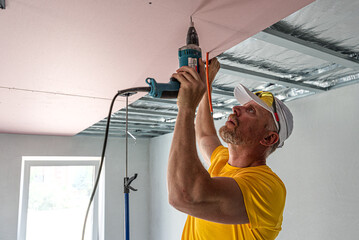 Wall Mural - The worker screwing plasterboard to the ceiling. He is using special electric screwdriver and drywall lift. A red plasterboard improve the fire resistance of ceiling structures.