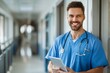 © Bilal Raza - Cheerful handsome surgeon doctor man in blue uniform holding digital tablet computer, looking at camera, smiling, posing for portrait in clinic hall