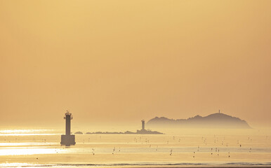 Spring and afternoon view of two lighthouses on the sea and reef against fog and island and horizon at Anmyeondo Island near Taean-gun, South Korea
