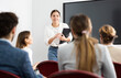 © JackF - Positive skilled female coach explaining topic to group of people during foreign language class in auditory