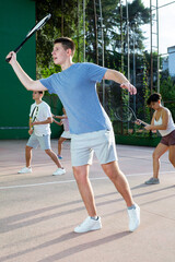 Wall Mural - Sporty young man playing popular team game frontenis at open-air fronton court on summer day, ready to hit rubber ball with racquet