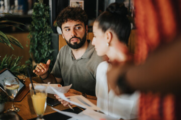 Wall Mural - Diverse group of people in a casual coffee bar setting collaborating and discussing business ideas while working with documents and laptops.