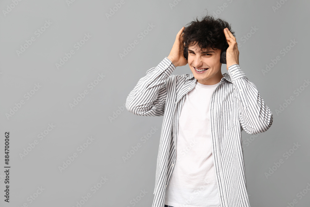 Handsome young man in stylish clothes and headphones on grey background