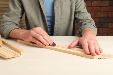 Man polishing wooden plank with sandpaper at table, closeup