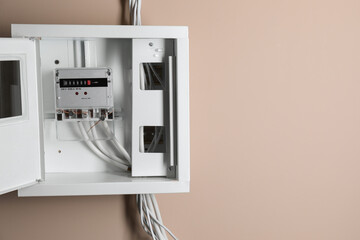 Electric meter in fuse box on beige wall, space for text. Energy measuring device