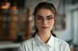 © anatolir - Confident young professional woman wearing glasses, with a sharp focus on her in an office setting